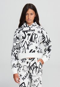 Felpa bianca con testo e grafiche in stile graffiti neri. Presenta un cappuccio con cordoncino e orlo a costine. Abbinata a pantaloni coordinati.