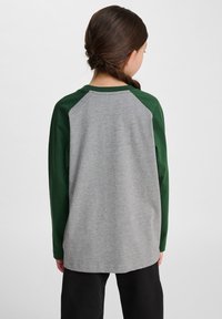 Langsleeve shirt met een grijze romp en donkergroene raglanmouwen. Zachte katoenmix, gebogen zoom en eenvoudige stikdetails.