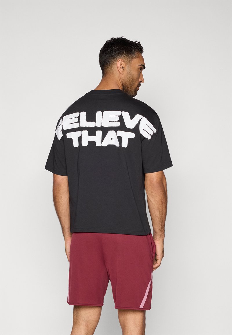 Čierne bavlnené tričko s bielym nápisom "VER V TOM" na chrbte, spárované s bordovými šortkami so svetloružovými bočnými pruhmi.