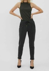 Mörkgrå, avsmalnande joggers med elastisk midja och dragsko. Köpt med en åtsittande grön ribbad linne och svarta högklackade skor.