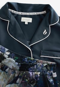 Conjunto de pijama de satén azul marino con ribete blanco. La parte superior tiene un bolsillo y un logo bordado; la parte inferior cuenta con una cinturilla elástica con estampado floral.