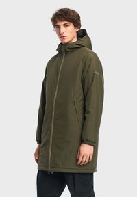 Parka vert imperméable avec capuche, fermeture éclair à l'avant, poignets élastiques et poches latérales. Texture lisse ; logo sur la manche.