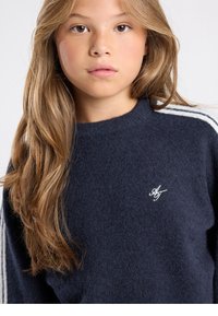 Pull en maille bleu marine avec col rond, rayures blanches sur les côtés et logo brodé sur la poitrine. Texture douce, coupe décontractée.