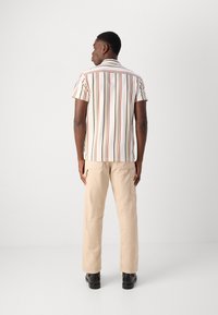 Chemise à manches courtes pour hommes avec des rayures verticales multicolores sur un fond clair, associée à un pantalon cargo beige et des bottes noires.