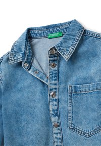 Camicia in denim azzurro chiaro con bottoni a pressione, colletto a punta, taschino sul petto e un'etichetta verde United Colors of Benetton all'interno del colletto.