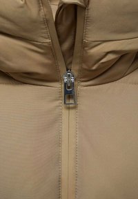 Beige pufferjack met een hoge kraag, glanzende stof en een centrale metalen rits. Het ontwerp bevat gestikte secties voor isolatie.