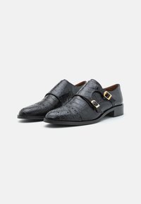 Schwarze Lederschuhe mit Krokodiloptik, ausgestattet mit doppelten Schnallen und perforierten Details sowie einem niedrigen Blockabsatz.