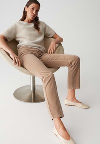 Pantaloni in corduroy beige con taglio dritto, abbinati a un maglione corto a maniche corte grigio chiaro in morbido tessuto e scarpe basse beige, seduto su una sedia girevole.