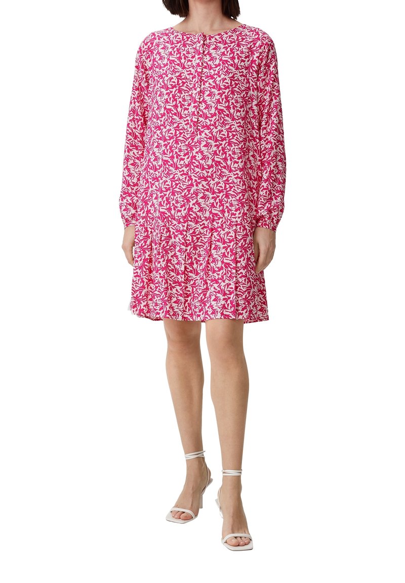 Femme portant une robe longue à manches longues rose et blanche à motif floral, longueur genou, avec des boutons et des sandales blanches à talons hauts et bride à la cheville.