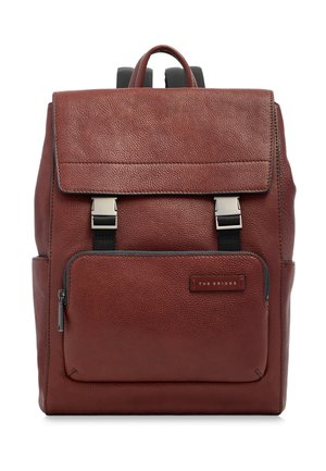 Zaino in pelle marrone con pattina superiore, tasca frontale con zip, due fibbie argentate e etichetta del marchio "The Bridge" sulla tasca.