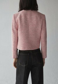 Lyserød tekstureret jakke med lange ærmer, cropped design og et subtilt mønster, parret med mørke denim jeans med baglommer.