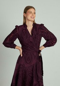 Rochie burgundy, cu mâneci lungi tip balon, cu un model floral texturat și o talie legată. Dantelă care se lărgește ușor la baza.