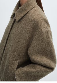 Brown wool blend coat featuring a collar, large pockets, and textured fabric with a soft finish. Slightly oversized design and dropped shoulders.