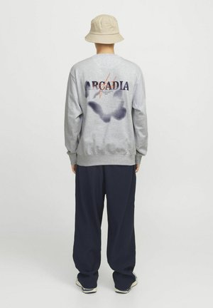 Grauer Sweatshirt mit 'ARCADIA'-Grafik und Fleckenmuster auf der Rückseite, kombiniert mit marineblauen Schlaghosen und einem beigen Bucket Hat.