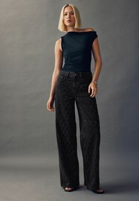 Fekete, bőszárú farmernadrág gyémántmintákkal és díszítésekkel, illeszkedő sötét tank toppal párosítva. Sima textúra és off-shoulder kialakítás.