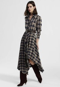 Vestito camicia a quadri scuri con orlo asimmetrico, maniche lunghe e cintura marrone. Presenta una chiusura con bottoni sul davanti e una texture del tessuto morbida.