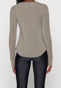 Světle taupe dlouhý rukáv top s kulatým lemem, detailem švu na zádech a úzkými rukávy, spárovaný s černými legínami. Měkká textilie.