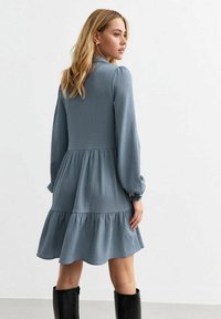 Blue textured dress with long sleeves, fitted bodice, and tiered skirt. Features a subtle checkered pattern and elasticized sleeve cuffs.