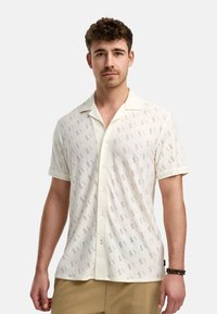Camicia a maniche corte con bottoni realizzata in tessuto bianco a trama con ritagli decorativi, caratterizzata da un colletto e bottoni frontali.