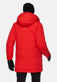 Parka rossa isolata con cappuccio, caratterizzata da una texture liscia, dettagli neri, polsini elastici e il logo del marchio sulla parte superiore della schiena.