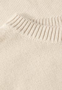 Sweter w kolorze kremowym, dziergany, z prążkowanym dekoltem, gładką fakturą oraz lekką konstrukcją z delikatnym, równomiernym wzorem ściegów.