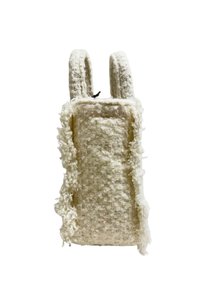 Sac tissé de couleur crème avec une surface texturée et des bords effilochés, doté de deux poignées robustes et arrondies pour le transport.
