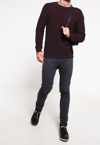 Burgundy strukturerad stickad tröja med rundad halsringning, kombinerad med mörka slim fit jeans och svarta skor. Svart axelväska som bärs över axeln.