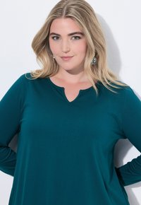 Taehlfarbendes Langarmshirt mit rundem Halsausschnitt und einem kleinen Ausschnitt in der Mitte. Weicher Stoff und lockere Passform.