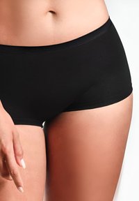 Shorts neri in cotone con design aderente, texture liscia e vita piatta. Colore della pelle visibile vicino ai bordi.