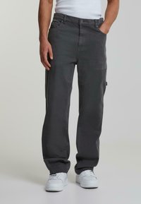Grå cargobukser laget av slitesterk bomull. Har flere lommer og en avslappet passform. Sammen med hvite joggesko på en nøytral bakgrunn.