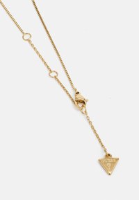 Goldene Halskette mit zartem Kettchen, ausgestattet mit einem dreieckigen Anhänger, der "GUESS" eingraviert hat, und einem Verschluss.