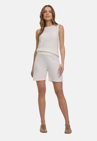 Top sans manches en tricot beige clair associé à un short assorti. Les deux présentent une texture à côtes verticales et une coupe décontractée. Agrémenté de détails minimalistes.