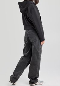 Černá oříznutá mikina s kapucí, spojená s volně střiženými tmavě šedými džíny. Outfit doplňují šedé sportovní tenisky.