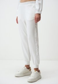 Witte joggingsbroek met een gladde textuur, elastische tailleband en zijzakken met rits. Gecombineerd met witte sneakers met beige accenten.
