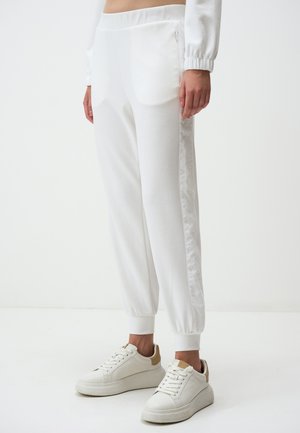 Pantaloni da jogger bianchi con una texture liscia, vita elastica e tasche laterali con zip. Abbinati a sneakers bianche con dettagli beige.