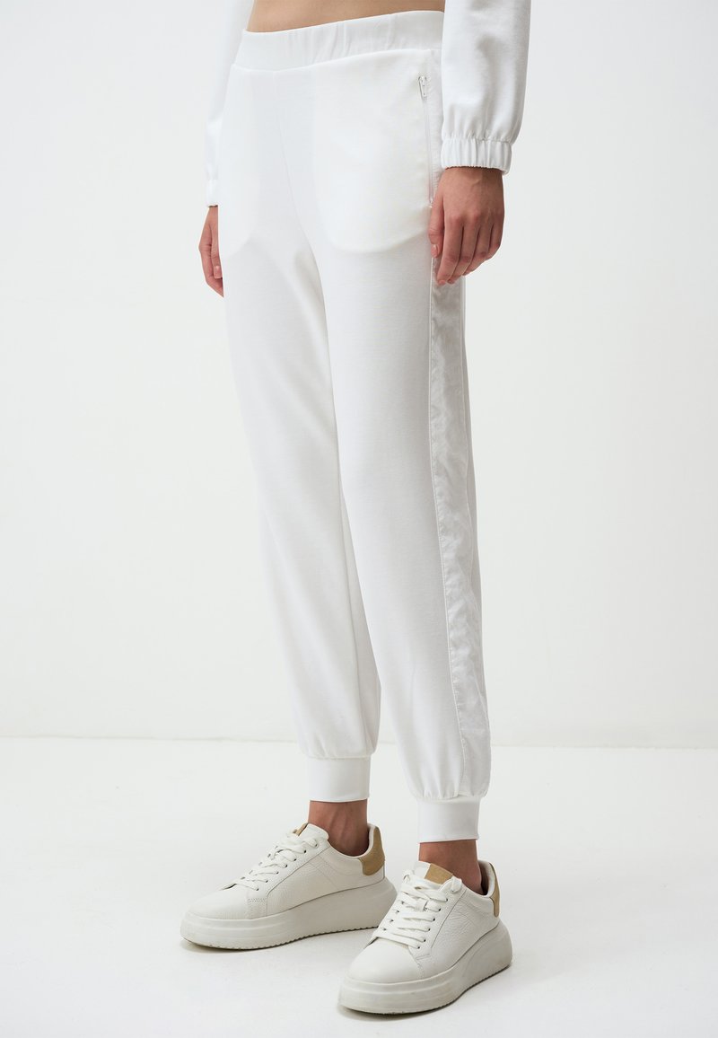 Witte joggingsbroek met een gladde textuur, elastische tailleband en zijzakken met rits. Gecombineerd met witte sneakers met beige accenten.