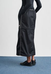 Μαύρη μονωμένη φούστα με ελαστική μέση και λευκές ρίγες, με πλαϊνές τσέπες και ταμπελάκι με λογότυπο, συνδυασμένη με μαύρα αθλητικά παπούτσια.