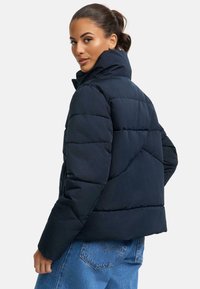 Marinblå puffjacka med hög krage, med kviltade sektioner och en kortad design. Slät textur och lätt vikt.