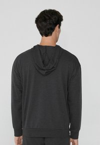Sudadera con capucha de color gris oscuro, cuenta con cordones, mangas largas y puños y dobladillo acanalados. La tela parece suave y texturizada.