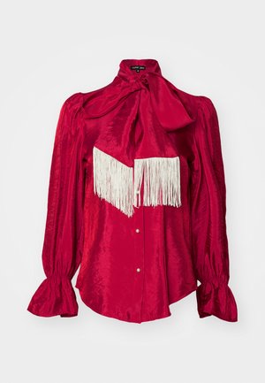 Punainen satiinipusero, jossa on korkea kaulus ja suuri nappi, pitkät puffihihat ja valkoinen fringedetaili rinnassa. Napitus edessä.