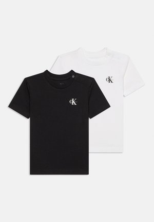 Mustvalged lühikeste varrukatega T-särgid CK logoga rinnal ja õlale kinnitatavate trukkidega, valgel taustal.