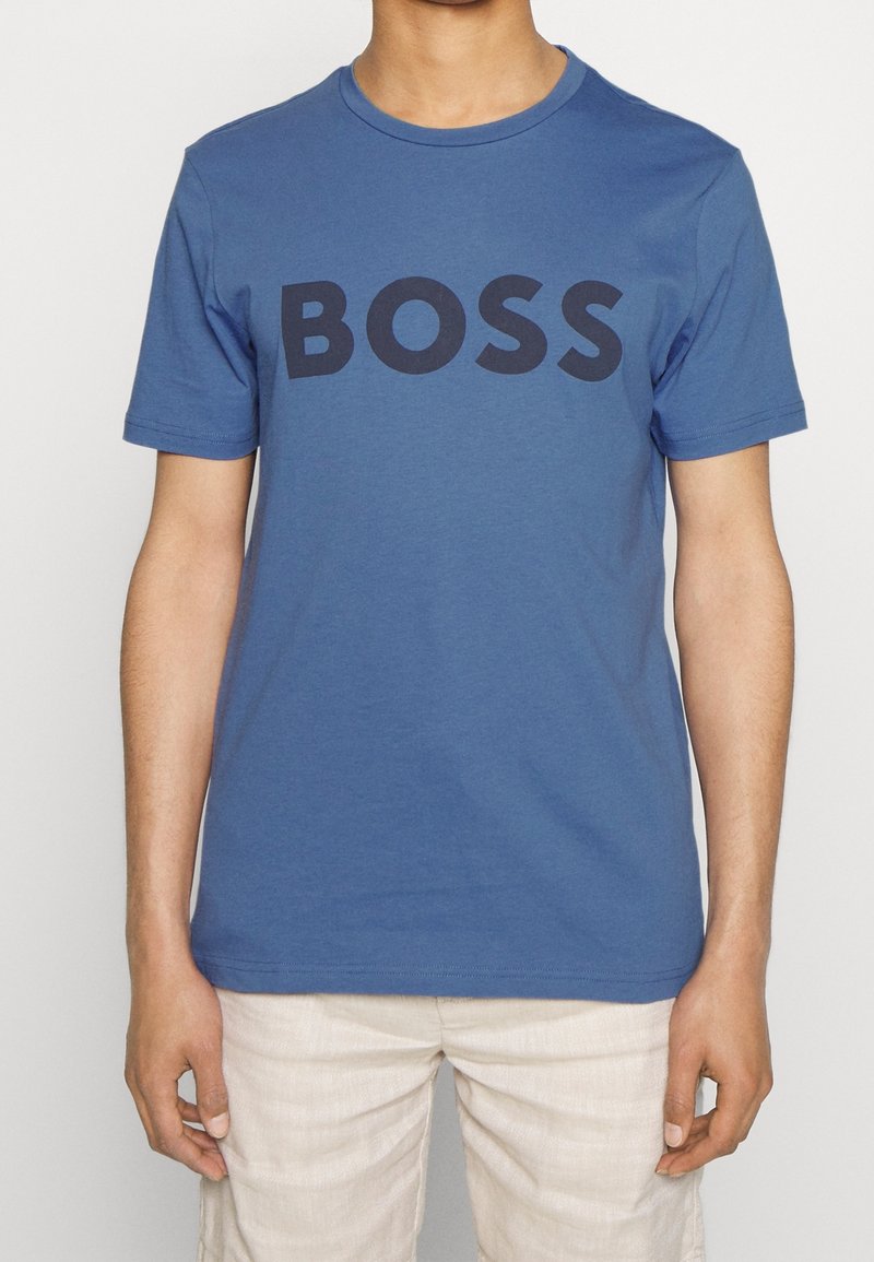 Blå bomullströja med ordet "BOSS" i fet svarta bokstäver över framsidan; korta ärmar och rundad halsringning.