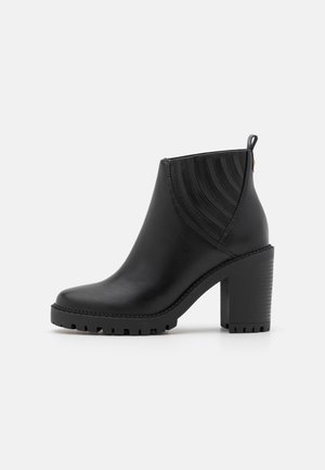 Bottine noire en cuir lisse, avec un talon épais, des accents ribbed sur les côtés et une semelle texturée avec un léger plateau.