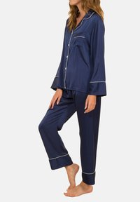 Ensemble de pyjama en satin marine comprenant un haut à boutons avec une poche et des manches larges, assorti à un pantalon avec des ourlets à revers et des passepoils contrastants.
