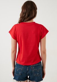 Rød kortærmet t-shirt med rund halsudsk�æring, der har en glat tekstur. Kombineret med denimshorts, der har frynsede kanter og baglommer.