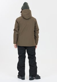 Olivgrön huva jacka, svarta isolerade byxor och mörka stövlar med låg profil. Slät textur, funktionell design, lämplig för utomhusbruk.