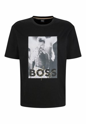 Sort T-shirt med korte ærmer med et sort-hvidt foto af en mand, der optræder, iført en jakke med nitter og seler, med teksten "BOSS" overlejret.