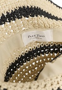 Gros plan sur un chapeau en paille tissé avec des rayures noires et une bande de tissu intérieure beige portant l'inscription "Part Two Est Copenhagen 1986".