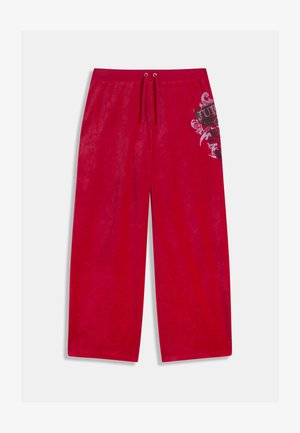 Punased laia lõikega dressipüksid, mis on valmistatud pehmest kangast ja millel on paelaga vöökoht. Paremal jalal on musta ja hõbedase värviga graafiline trükk.