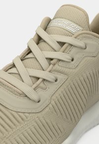Beige színű sneaker, textúrázott hálós felsőrésszel, kerek orral, rugalmas fűzőkkel és minimalista dizájnnal ellátott fehér gumitalppal.